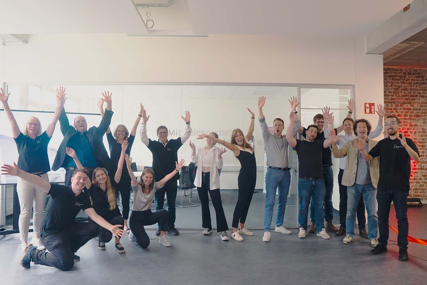 Das Team des Gründungszentrums, bestehend aus mehreren Personen, reißen glücklich die Hände in die Höge und lächeln in die Kamera.